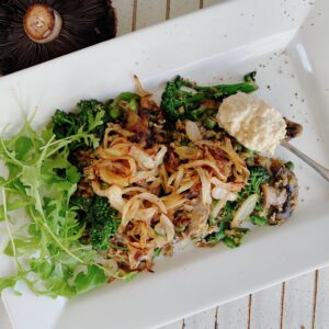 A nutritious plate of freekeh cooked with green peas and mushrooms, topped with fresh rocket, caramelized onions, hummus, and a sprinkle of thyme.