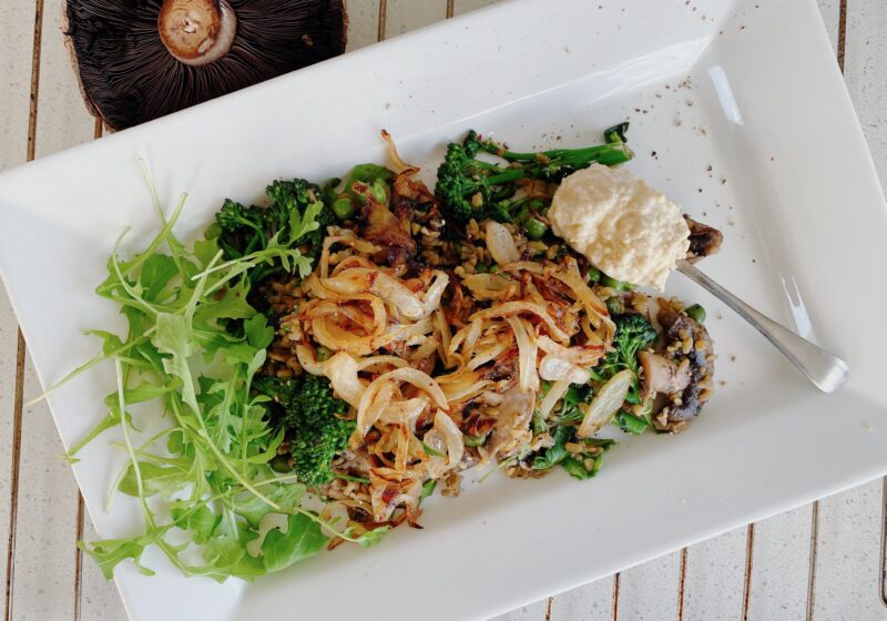 A nutritious plate of freekeh cooked with green peas and mushrooms, topped with fresh rocket, caramelized onions, hummus, and a sprinkle of thyme.
