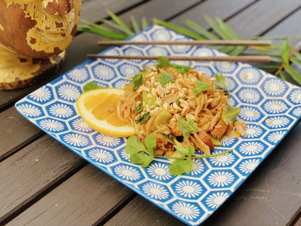 A vibrant plate of Pad See Ew highlights tofu, cilantro, noodles, and a sprinkle of peanuts against a backdrop of classic Thai aesthetics.