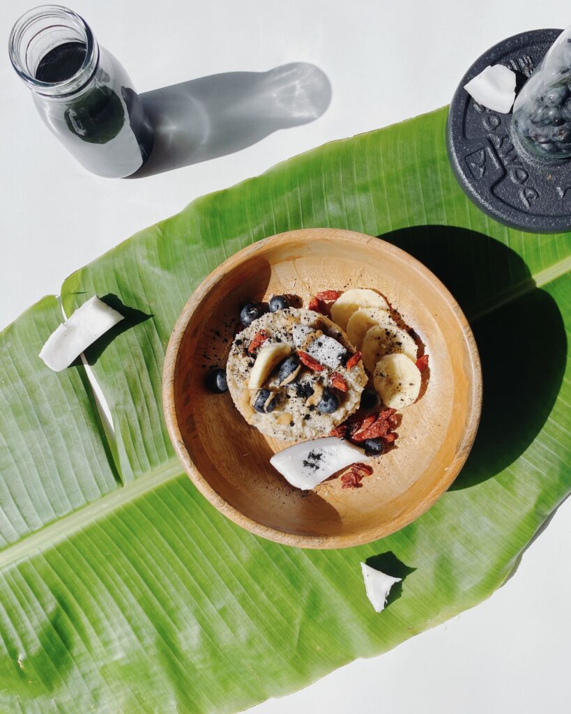 A bowl of vegan oats topped with goji berries, blueberries, and crunchy coconut, served on a vibrant green banana leaf.