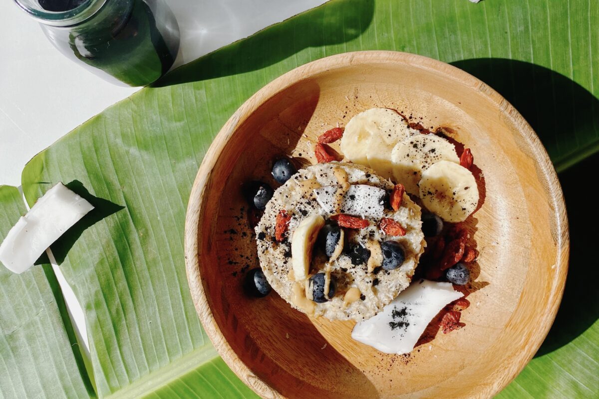 A bowl of mixed berries (blueberries and goji berries), shredded coconut, and oats served on a banana leaf, accompanied by pieces of charcoal on the side.