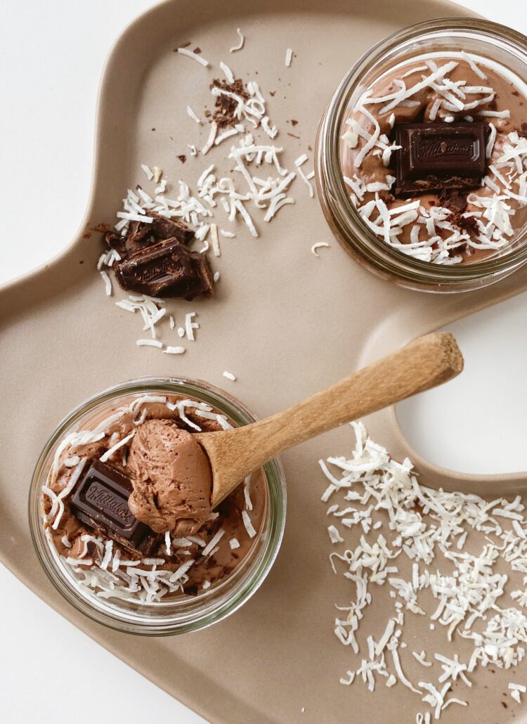 Two jars of chocolate mousse with coconut shavings on a tray.