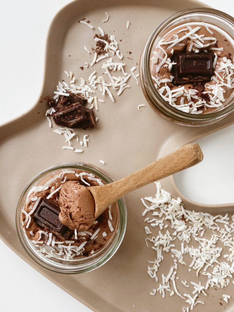 Two jars of chocolate mousse with coconut shavings on a tray.