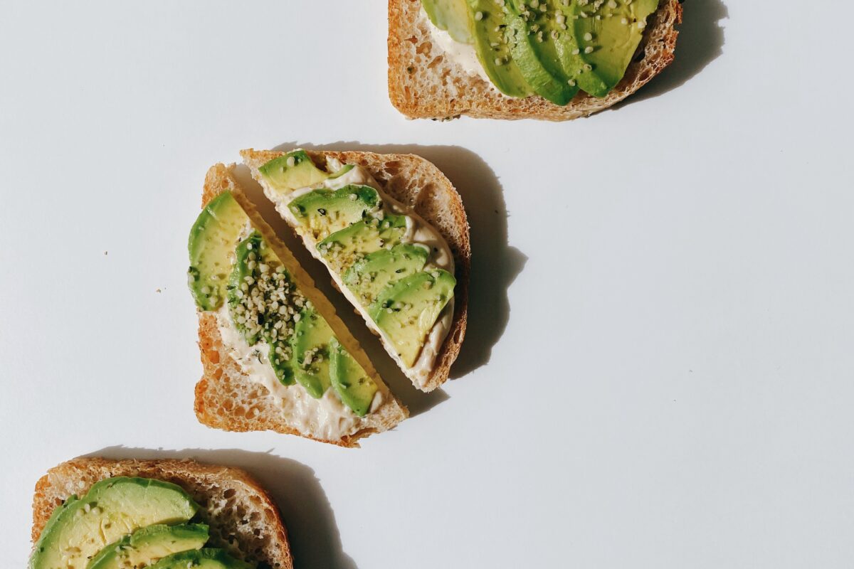 Three slices of delicious avocado toast served on a clean white surface topped with hemp seeds.