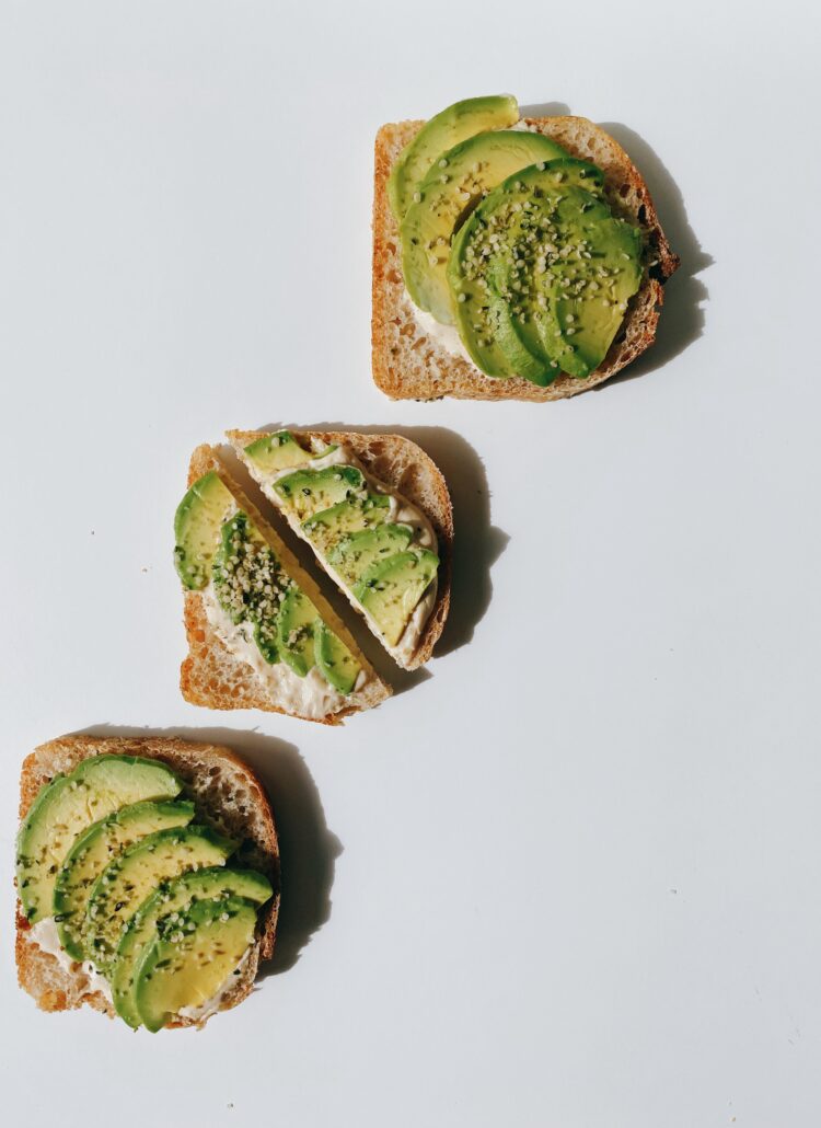 Three slices of delicious avocado toast served on a clean white surface topped with hemp seeds.