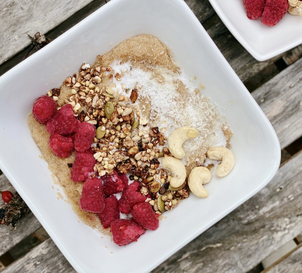 The image features a captivating arrangement of a nourishing bowl filled with superfood amaranth grains, topped with a colorful bounty of fresh, plump raspberries. The vibrant red hues of the raspberries pop against the creamy backdrop of the amaranth, creating an irresistible visual treat. The dish is beautifully presented on a rustic wooden table, exuding warmth and natural charm. 