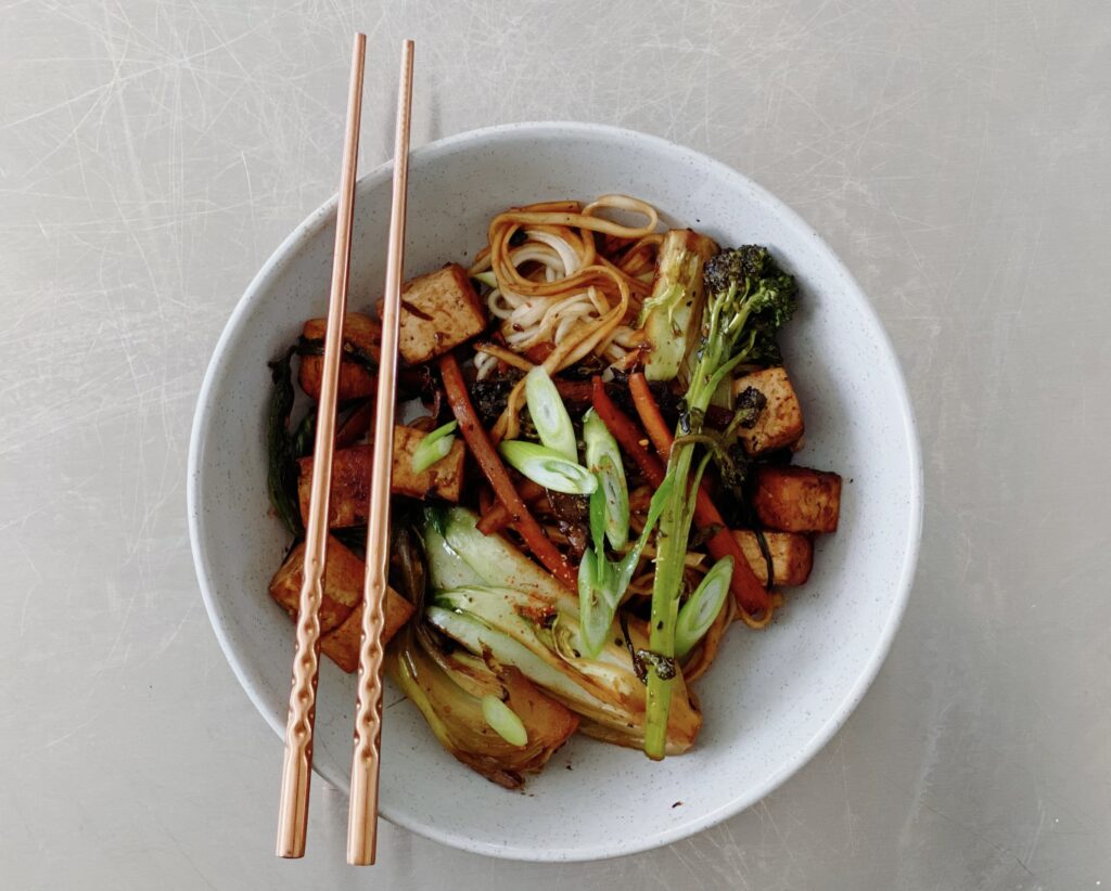 A vibrant bowl of noodles garnished with vegetables and accompanied by chopsticks.