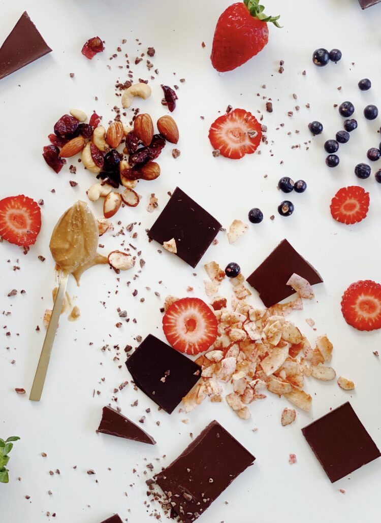 An image showcasing a delicious assortment of chocolate, fresh strawberries, blueberries, and scattered granola bits and bobs