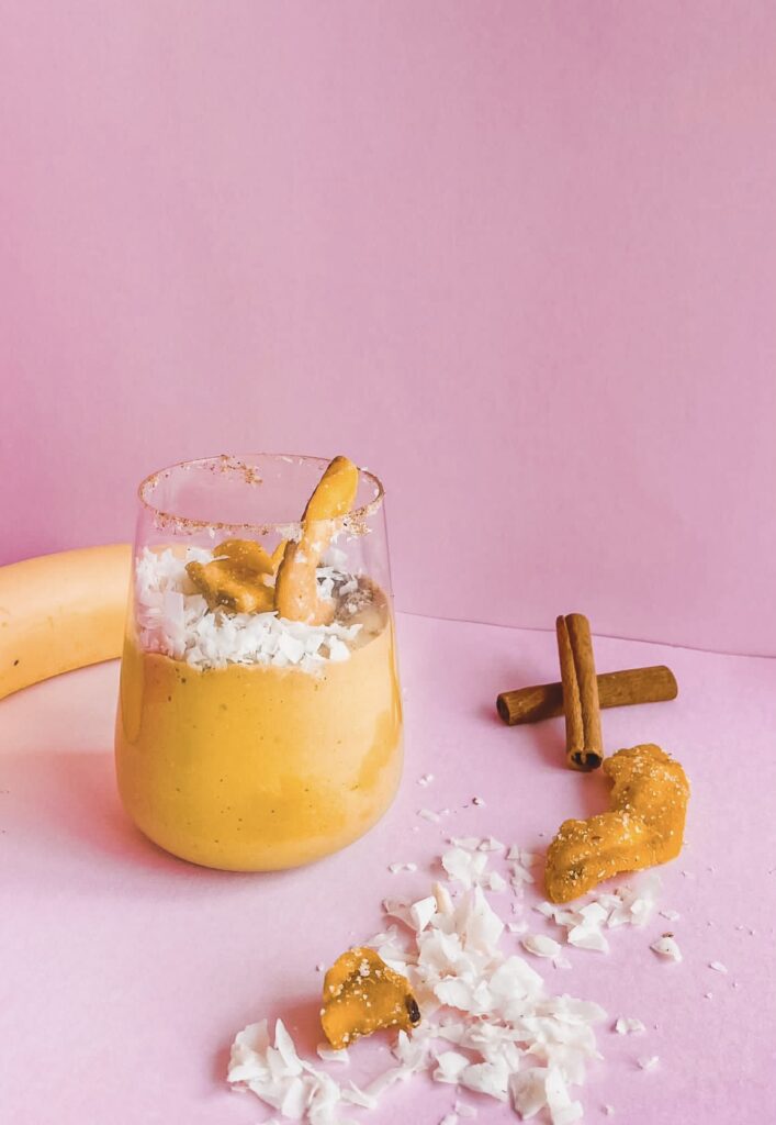 A banana and maca smoothie with cinnamon and coconut on a pink background.