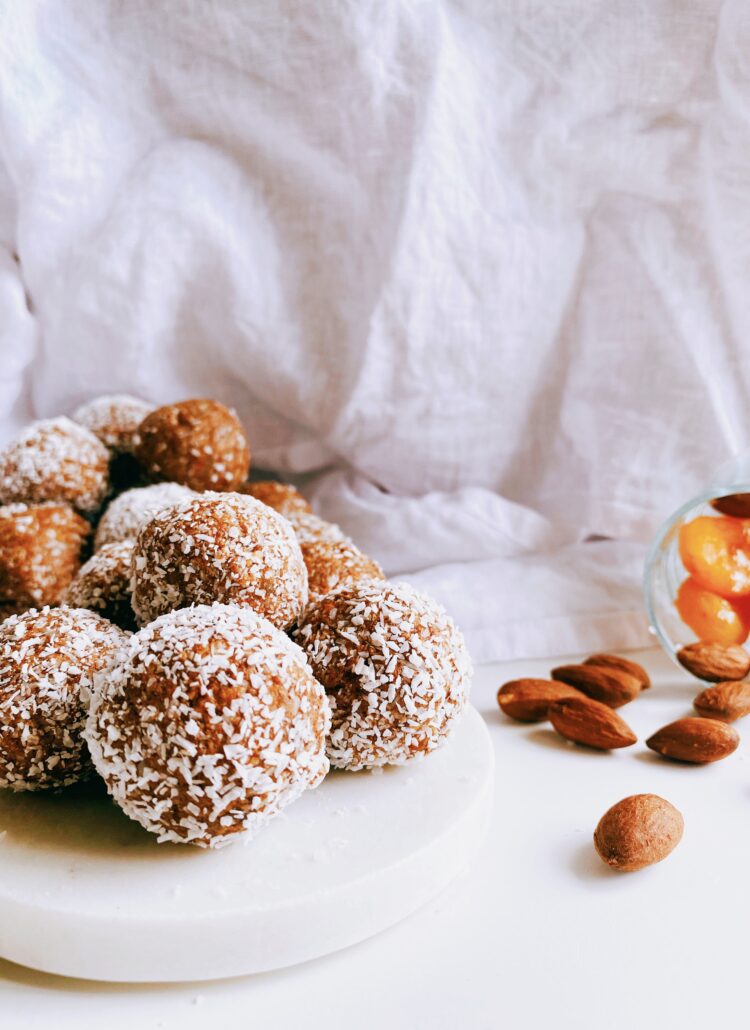 A plate showcasing Apricot Bliss Balls, protein-rich energy balls, and a side bowl filled with ingredients including almonds and apricots.