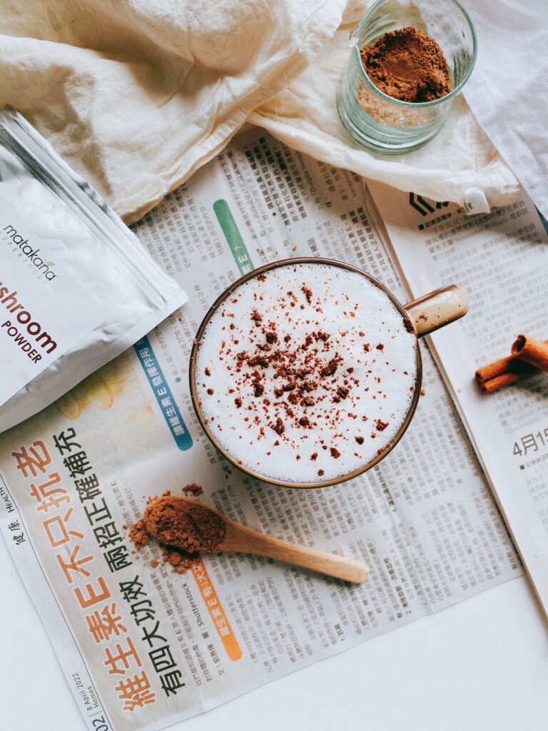 Enjoy a warm and aromatic treat: A newspaper holds a reishi mushroom latte served in a cozy mug, topped with frothy milk and accompanied by a cinnamon stick for an extra touch of flavor.
